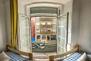 A room with a curved glass door leading to a balcony. The balcony has a metal railing and overlooks a parking area with several cars. - FORTUNE GUESTHOUSE (Lisbon)
