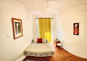 Een slaapkamer met een bed, een klein nachtkastje, een stoel en een raam met gordijnen.