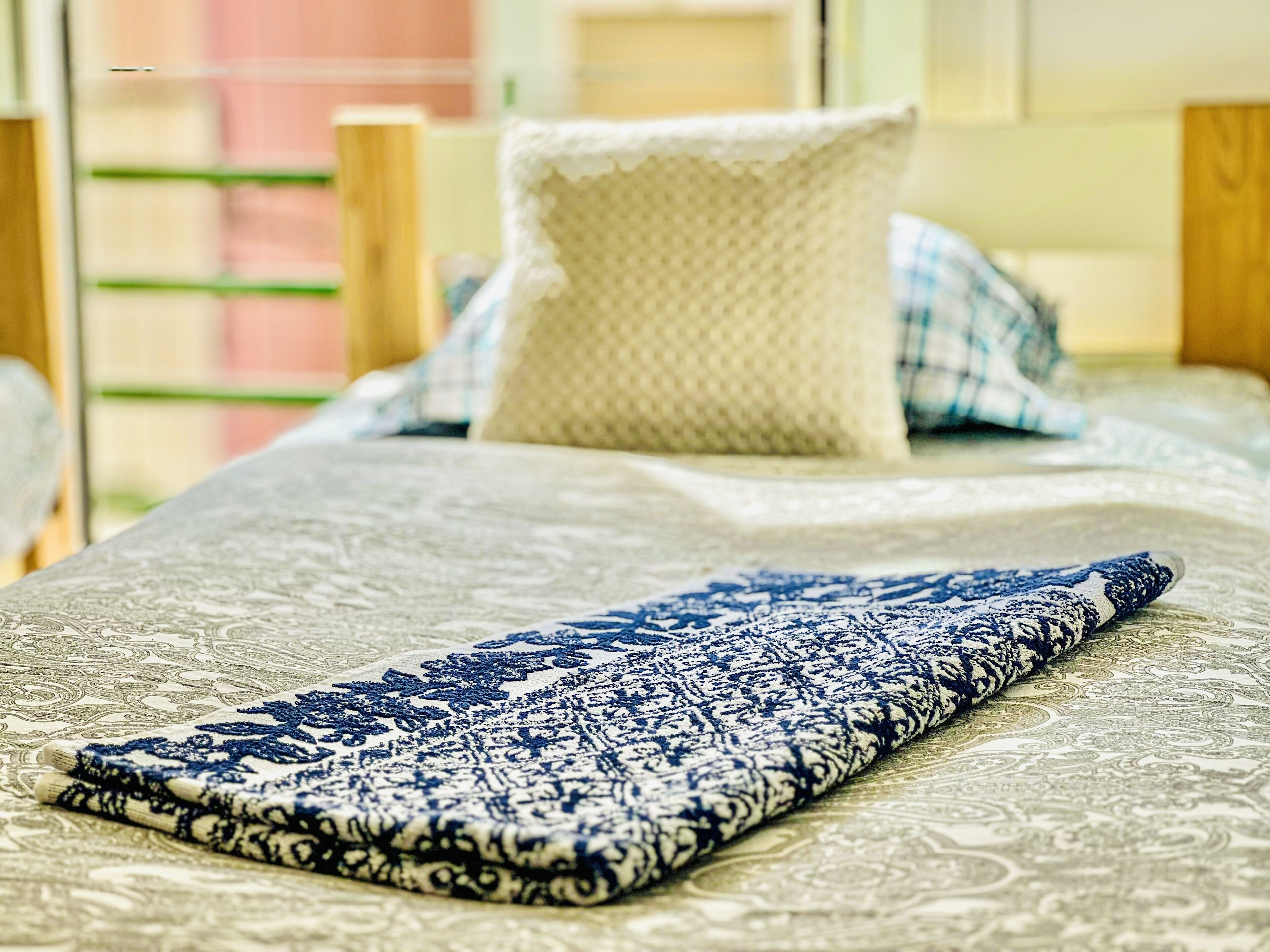 A neatly made bed with a patterned bedspread and a blue and white throw blanket.