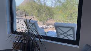 Una habitación con ventana que da a un paisaje desértico, una mesita con una planta y una silla.