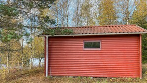A red wooden cabin with a small window, surrounded by trees and a forested area. - Stunning home in Ambjörnarp with WiFi (Ambjörnarp)