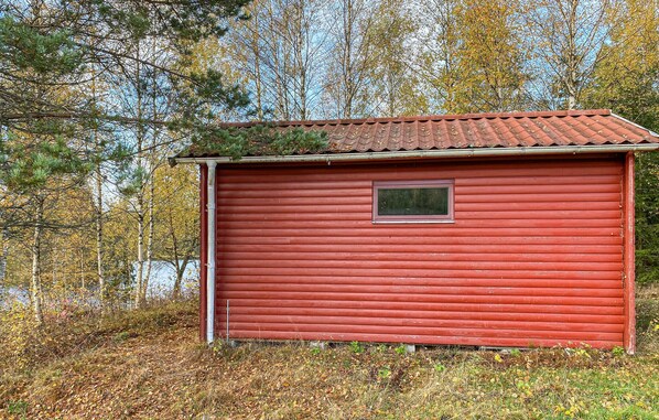 A red wooden cabin with a small window, surrounded by trees and a forested area. - Stunning home in Ambjörnarp with WiFi (Ambjörnarp)