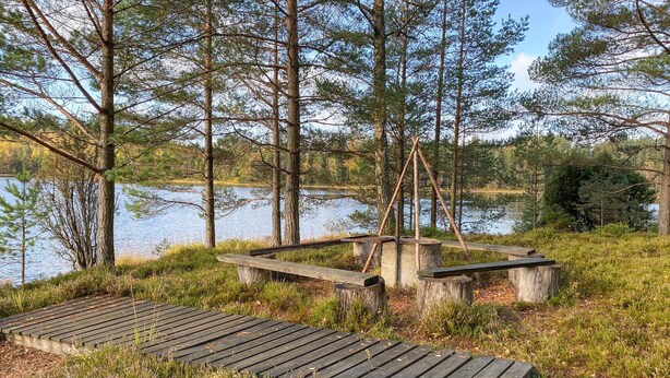 A wooden deck with benches overlooking a lake, surrounded by tall trees and grassy areas. - Stunning home in Ambjörnarp with WiFi (Ambjörnarp)