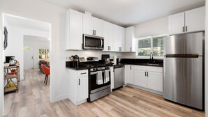 A modern kitchen with white cabinets, stainless steel appliances, and a wooden floor.
