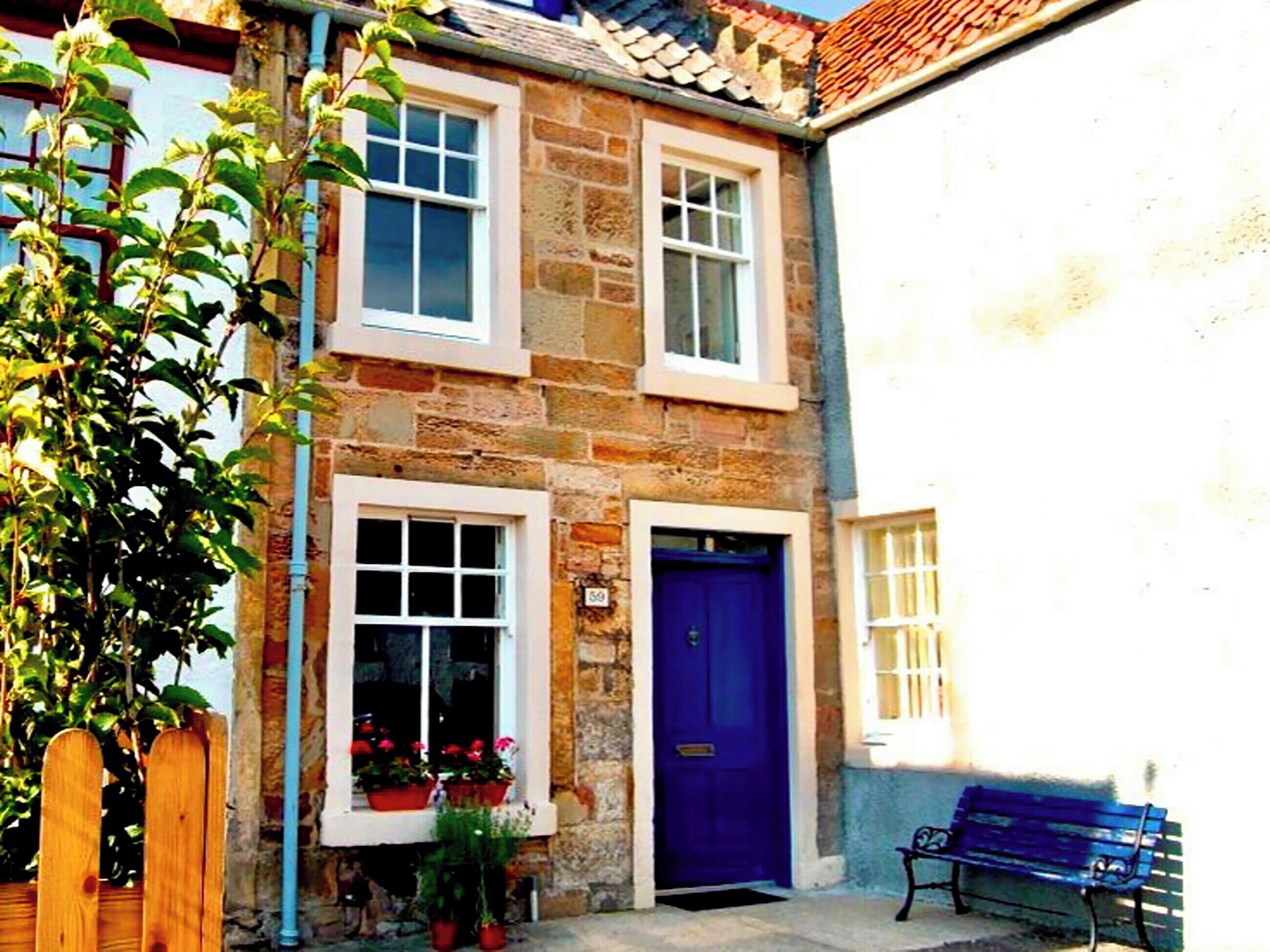 A stone building with a blue door and windows, a wooden fence, and a bench.