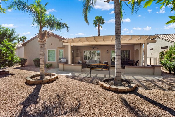 A covered patio area with a seating arrangement, palm trees, and a gravel ground.