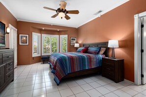Quarto com cama, mesas de cabeceira, ventilador de teto e janela com persianas.