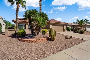 A residential house with a tiled roof, palm trees, and a gravel driveway.