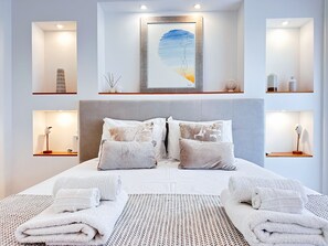 Une chambre d’hôtel moderne avec un grand lit, de nombreux oreillers, une œuvre d’art encadrée au-dessus du lit et des étagères intégrées ornées d’objets décoratifs.
