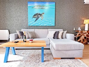 A living room with a grey sofa, a wooden coffee table, and a painting of a sea turtle.
