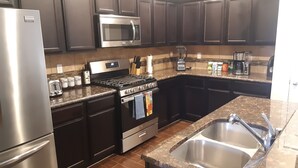 A modern kitchen with dark cabinetry, stainless steel appliances, granite countertops, and a double sink.