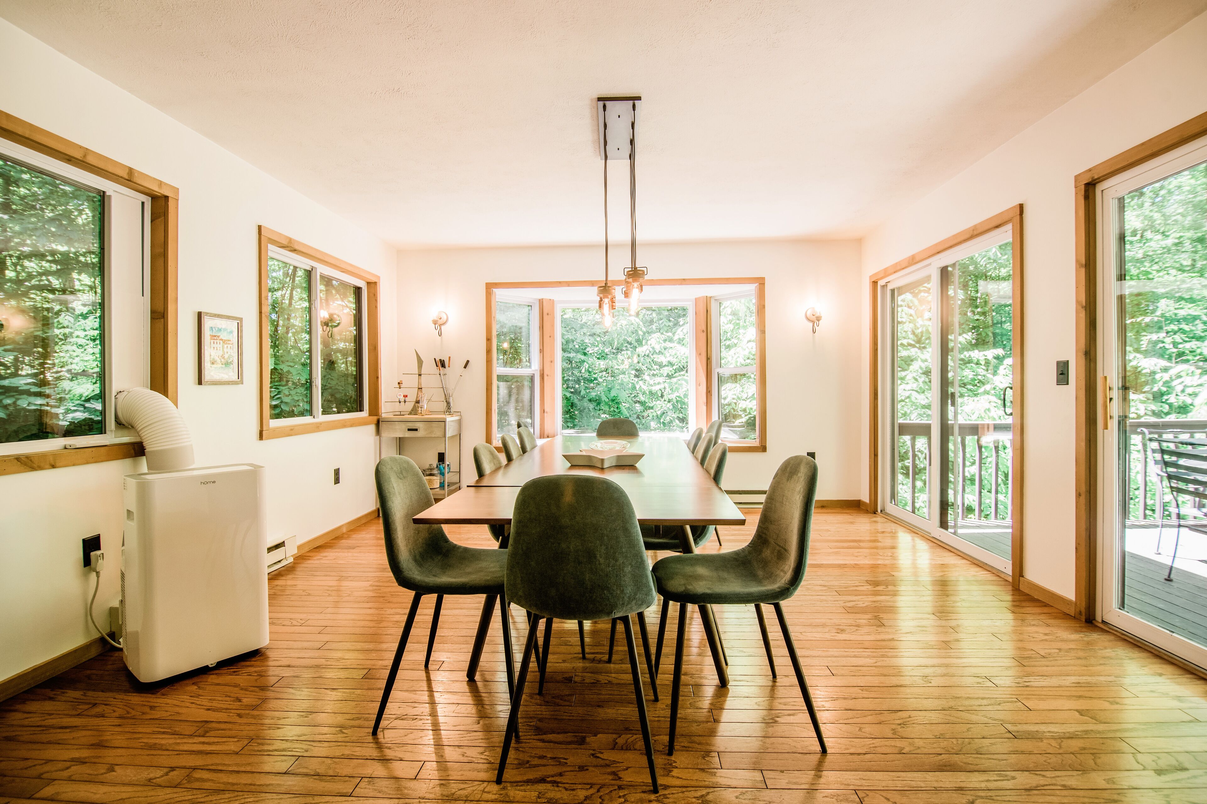 A dining area with a long table, six chairs, and a modern chandelier.