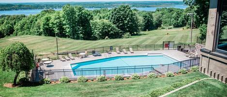 A swimming pool with a view of a lake, surrounded by a fenced patio area with lounge chairs.