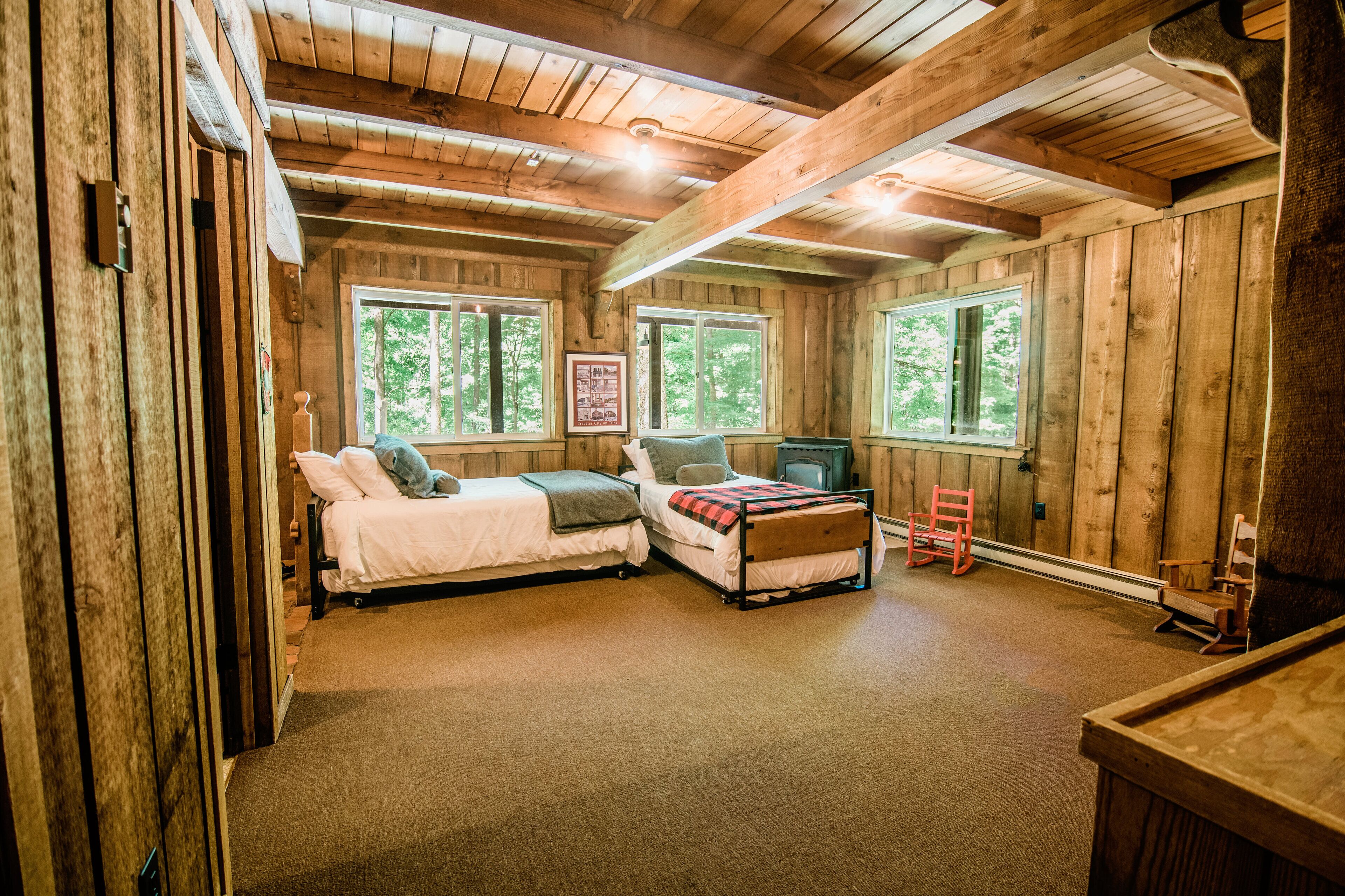 L'intérieur d'une cabane comprenant deux lits, une cheminée et de grandes fenêtres.