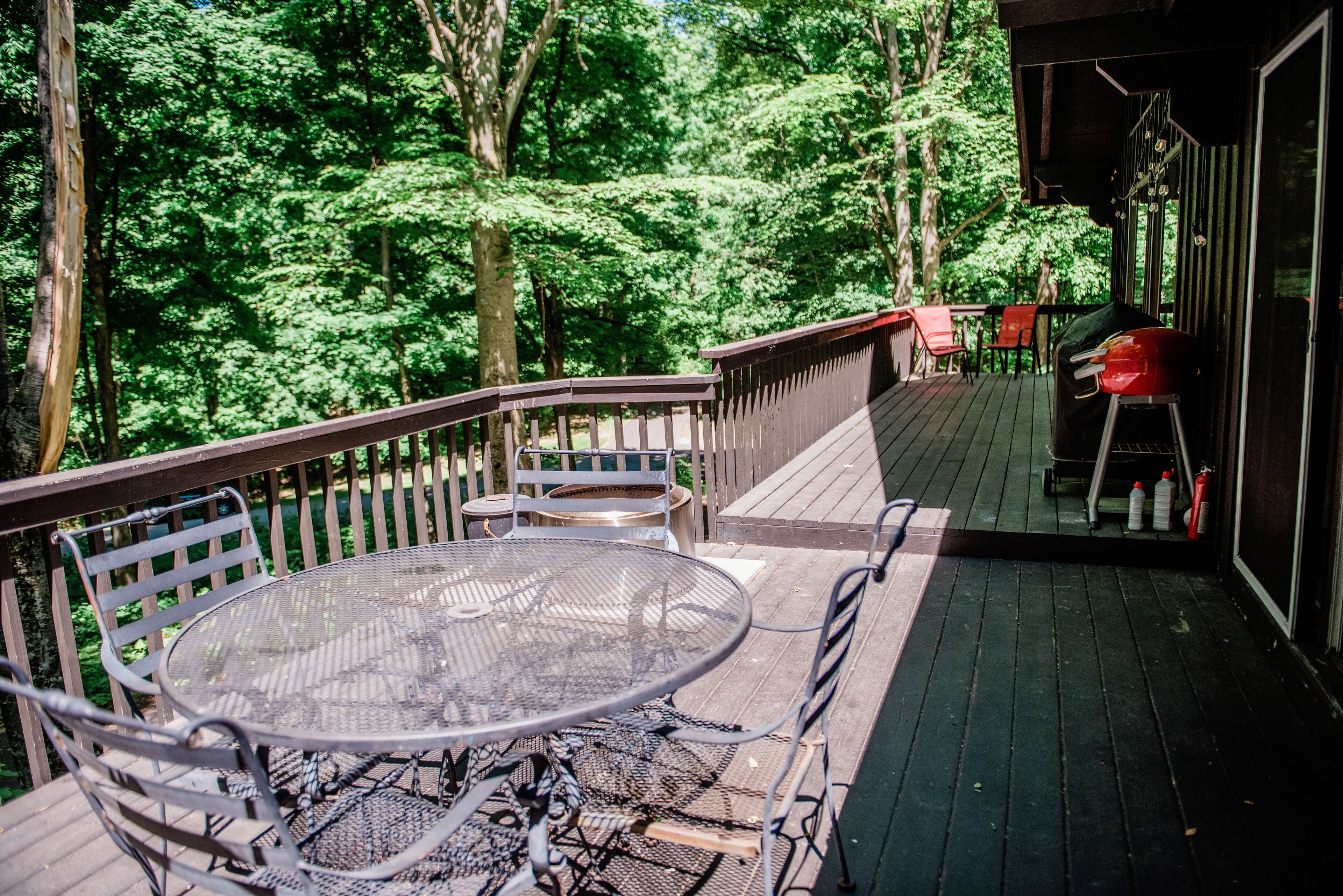 Une terrasse en bois avec une table et des chaises en métal, entourée d’arbres.