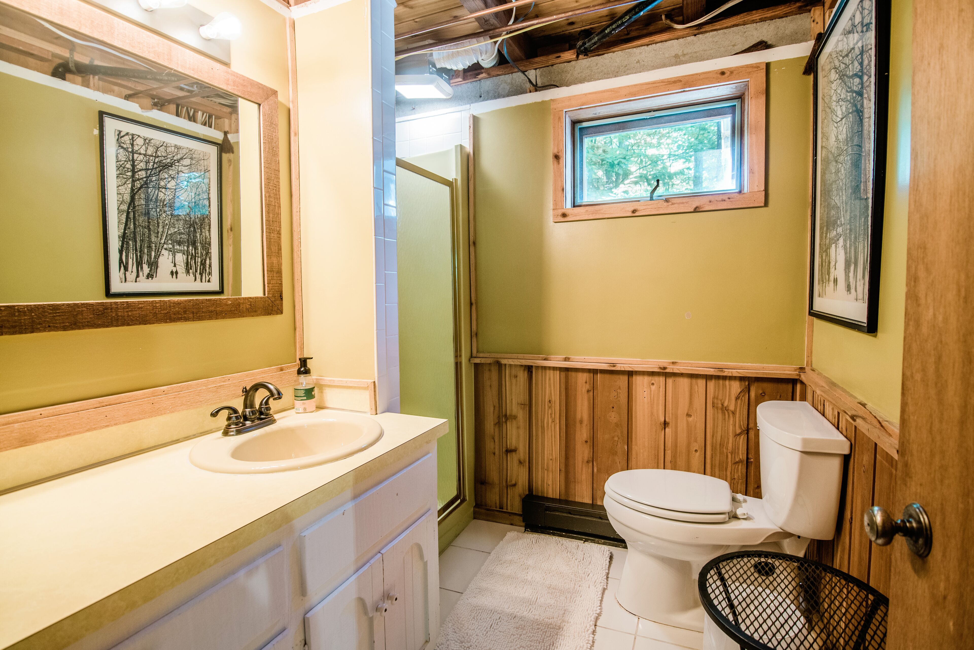 Ein Badezimmer mit einem Holzkosmetikschrank, einem Waschbecken, einer Toilette und gerahmten Bildern an der Wand.