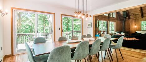 Un espace repas avec une table et des chaises en bois, de grandes fenêtres et une vue sur l’extérieur.