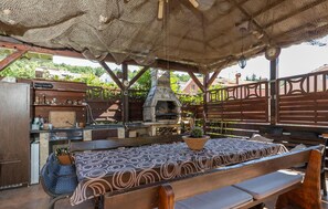 Eine Terrasse im Freien mit Kamin aus Stein, Holzmöbeln und einer Pergola darüber.