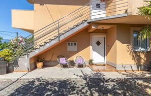 Ein modernes, zweistöckiges Haus mit einer Treppe, die zum Obergeschoss führt. Vor der Haustür stehen zwei Korbstühle mit Kissen.