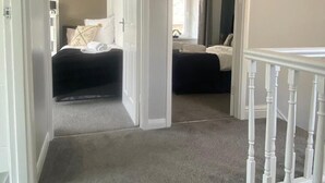 Een hal met vloerbedekking die leidt naar twee slaapkamers, elk met een bed en een raam.