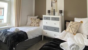 Een slaapkamer met twee bedden, een witte dressoir, een schilderij aan de muur en een raam met gordijnen.