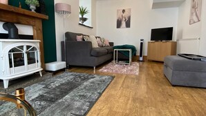 Een moderne woonkamer met een grijze bank, een witte kast, een televisie en een houten vloer.