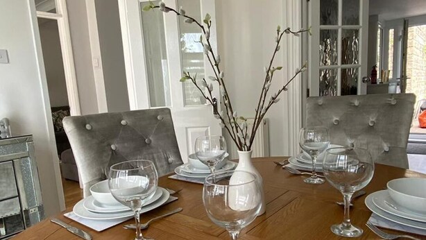 Een eettafel gedekt met witte borden, kommen en wijnglazen, met een vaas takken in het midden.