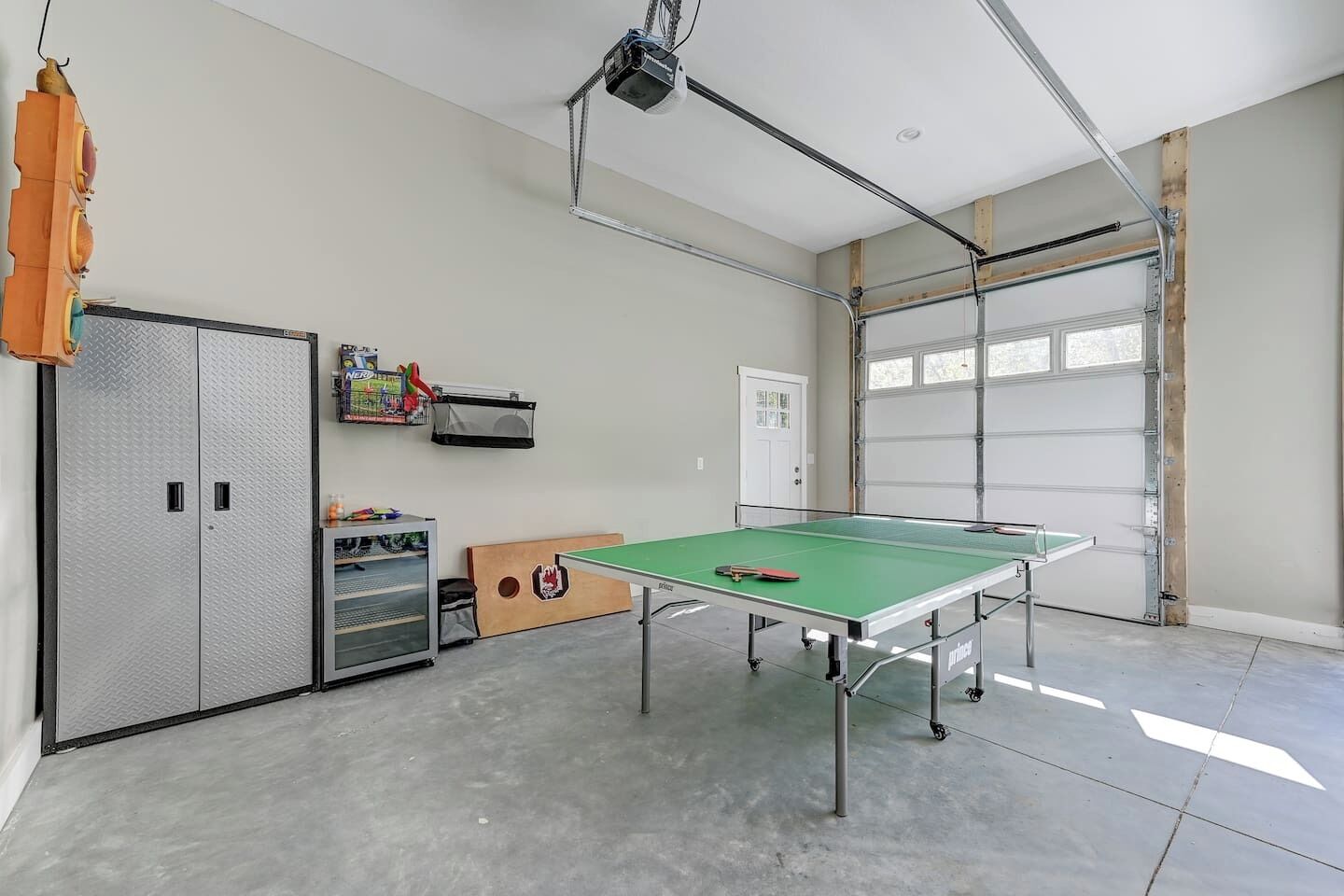Un espacio interior amplio con mesa de ping pong, un armario metálico y una puerta de garaje.