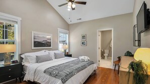 Une chambre à coucher comprenant un lit, des tables de chevet, un ventilateur de plafond, une fenêtre et une salle de bain.
