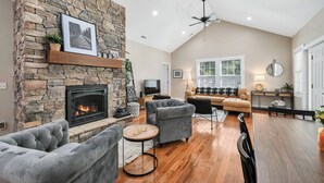 Un salon avec une cheminée en pierre, un ventilateur de plafond, un ensemble de canapés et un téléviseur.