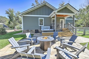 A house with a patio area featuring Adirondack chairs, a fire pit, and a hot tub.