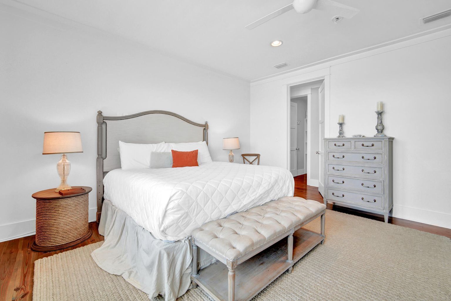A bedroom with a bed, bedside tables, a bench, a dresser, and a door.