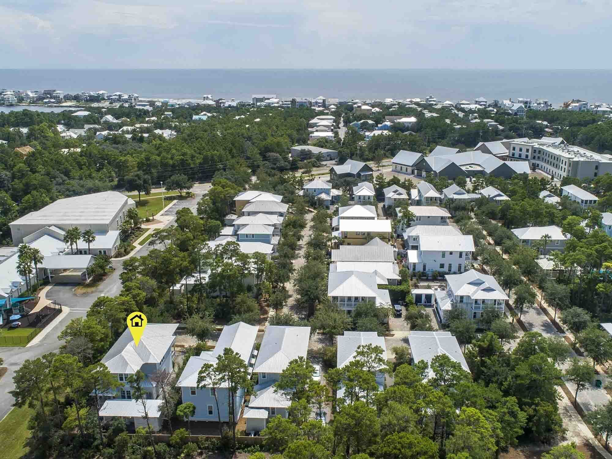 A residential area with detached houses, a large building with a flat roof, and a body of water in the background.
