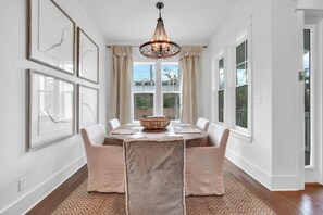A dining area with a round table, beige chairs, a chandelier, and framed artwork on the walls.