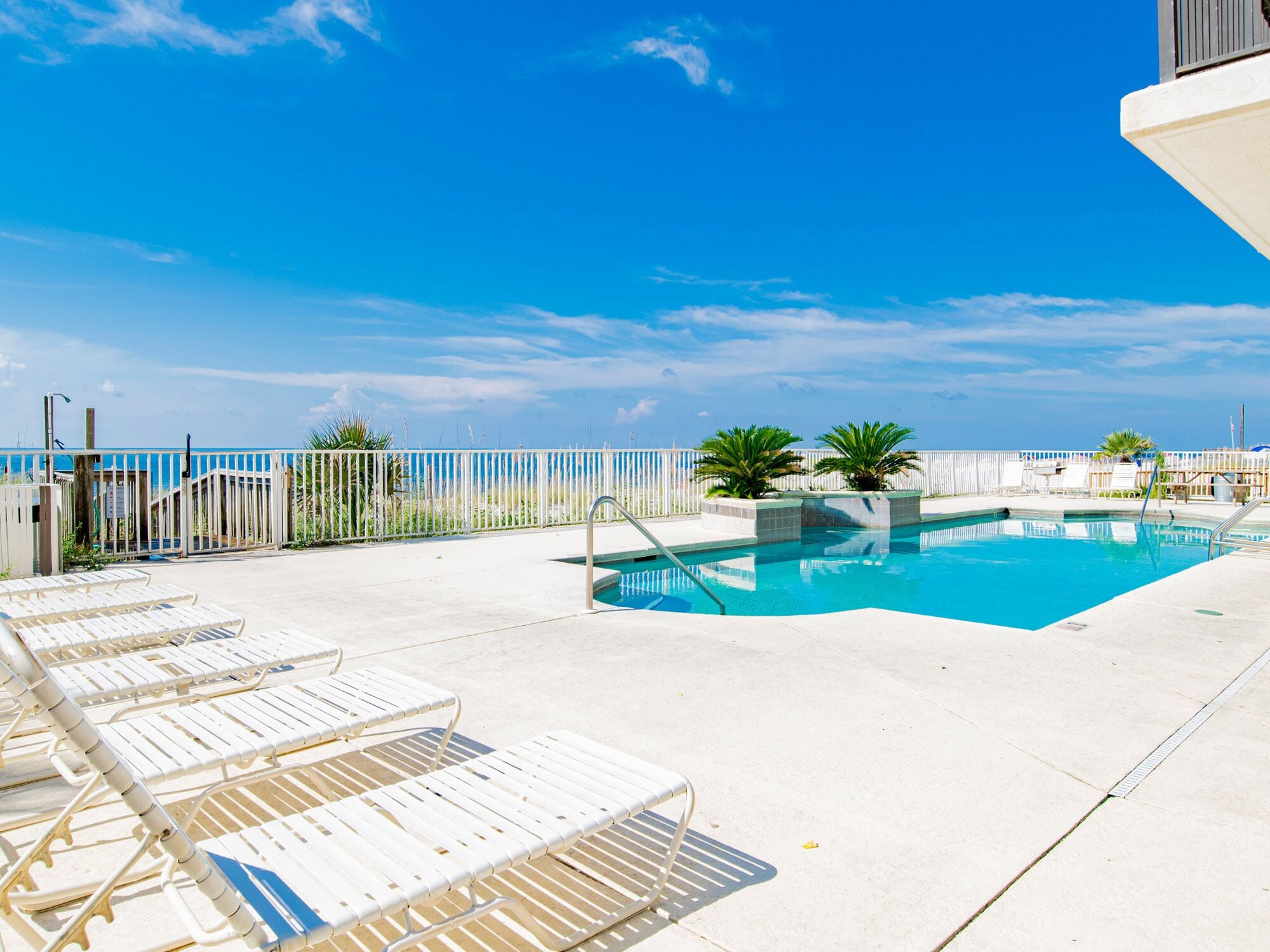 A pool area with lounge chairs and a clear view of the ocean.