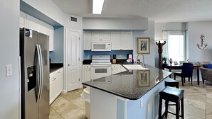 A modern kitchen with white cabinets, a stainless steel refrigerator, a built-in oven, and a large island with bar stools.