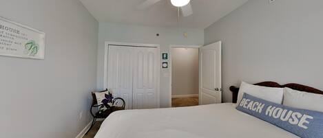 A bedroom with a bed, a ceiling fan, a sign on the wall, and a door leading to another room.