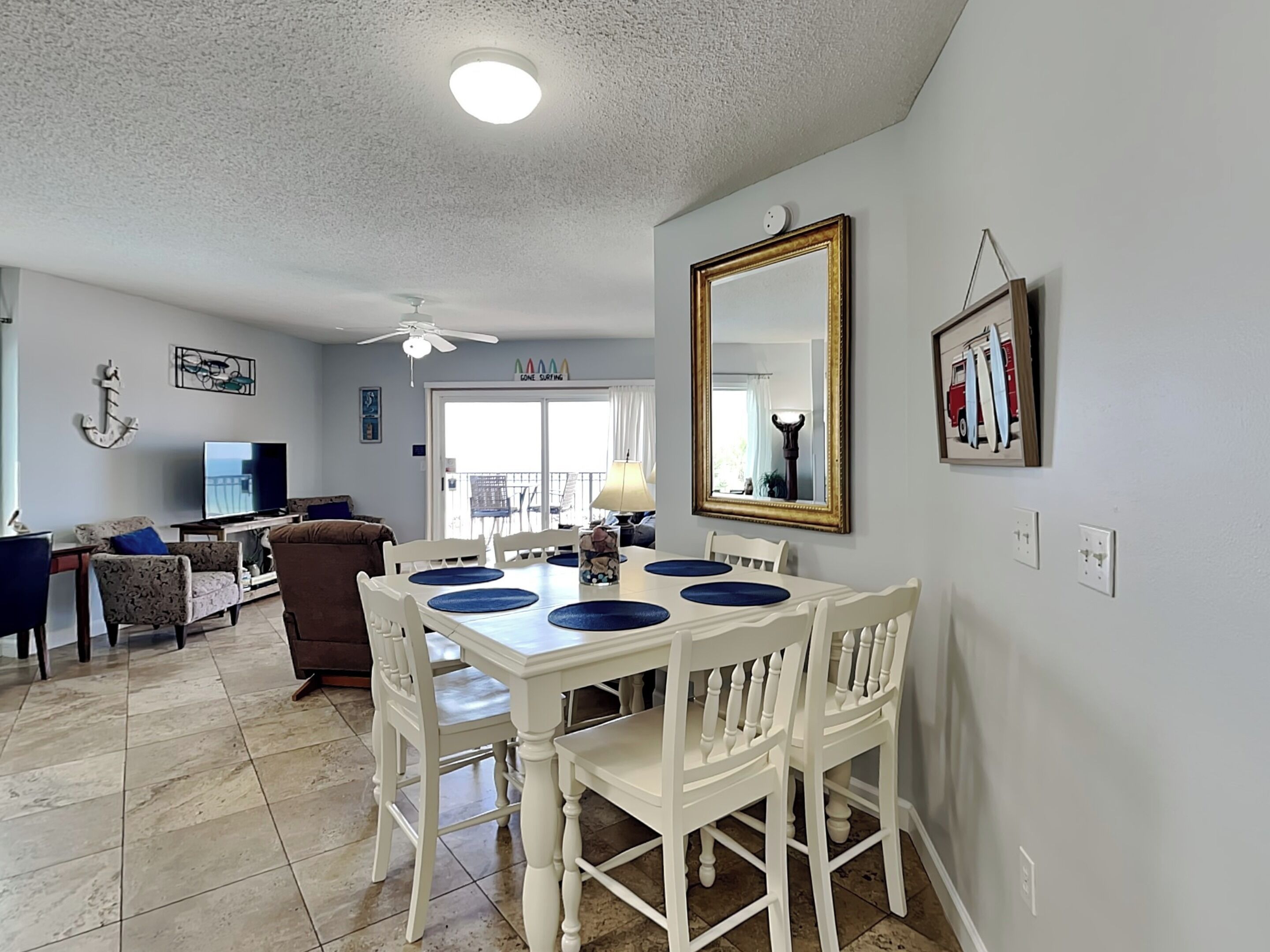 A dining area with a white table and chairs, a ceiling fan, and a large mirror on the wall.