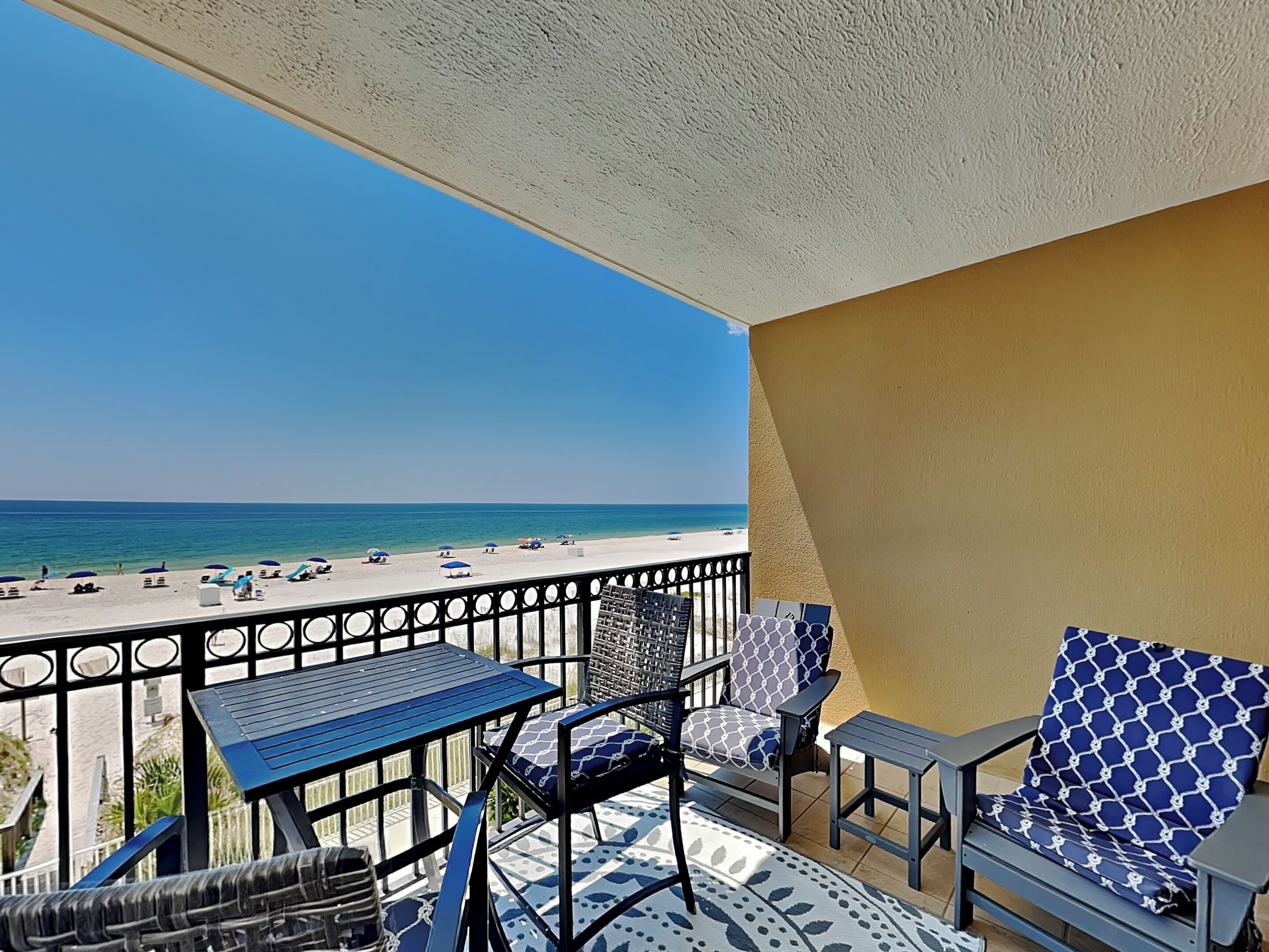 Un balcon avec vue sur la plage, des meubles d’extérieur et un ciel dégagé.