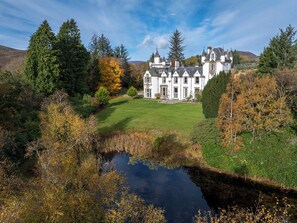 A large stately building with multiple towers, surrounded by a lush landscape and a small pond.