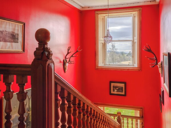 A staircase with a wooden railing, a red wall, a window with a view, and a chandelier.