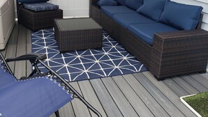 A covered outdoor patio with a wicker sofa, a chair, and a small table. - Cottage setup (New Bedford)