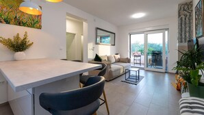 Ein modernes Wohnzimmer mit Essbereich, einer Sofagarnitur, einem Couchtisch und Blick ins Freie durch eine Glastür.