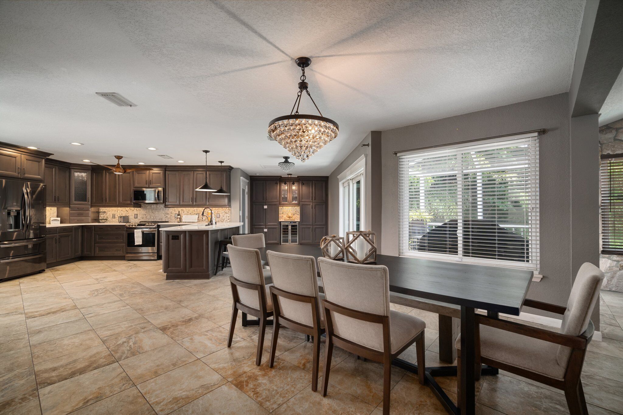 A modern kitchen with dark wood cabinets, a central island, and a dining area with chairs.
