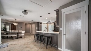 Een moderne keuken met een centraal eiland, barstoelen, hanglampen en een grote deur.