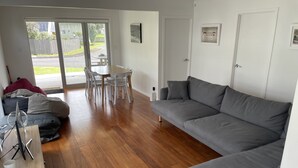 Ein modernes Wohnzimmer mit grauem Sofa, Holzboden, einem Esstisch mit Stühlen und einer Schiebeglastür, die auf eine Terrasse führt.