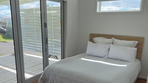 Ein Schlafzimmer mit Bett, Holzboden und einer Glastür, die zu einem Außenbereich führt.