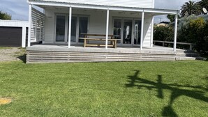 Ein modernes Haus mit einer Veranda, einer Holzbank und einem Rasen.