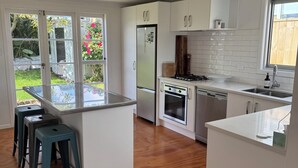 Eine moderne Küche mit weißen Schränken, einem Edelstahlkühlschrank, einem Backofen und einem Gasherd. Es gibt Hocker und eine kleine Kochinsel mit Spüle.