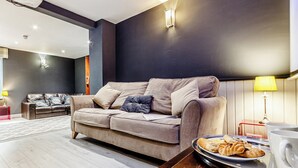 Ein modernes Wohnzimmer mit einem beigefarbenen Sofa, einem Couchtisch mit Gebäck und einer Lampe.